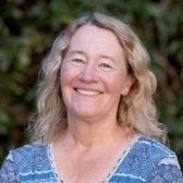 Headshot of research professor Carol Greider, PhD, in a blue and white striped blouse.