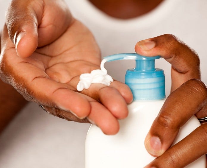 close up set of hands squeezing lotion from a pump dispenser