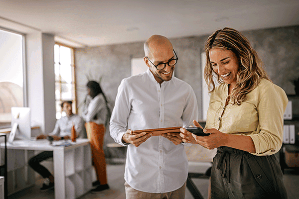 Two colleagues smiling and looking at a phone in a modern office.