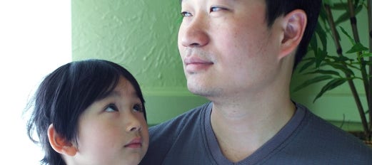 little girl sits in her father's lap and looks up at him