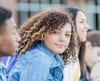 Teenage girl sitting in a row with her friends wearing a blue jean jacket and looking toward the camera