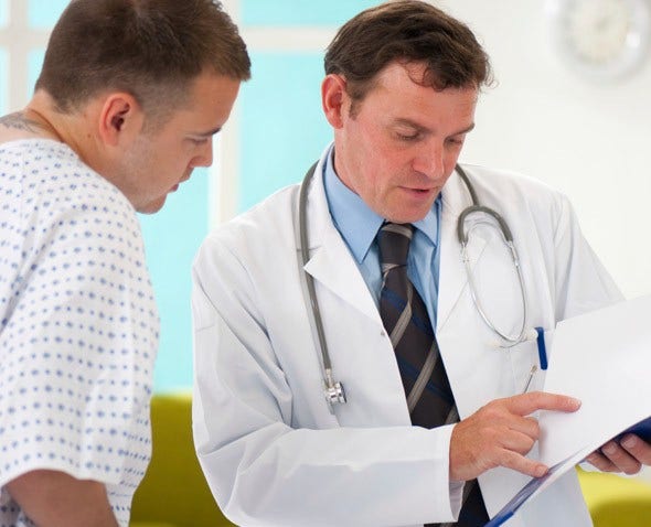 a doctor goes over paperwork with a patient in gown in an exam room