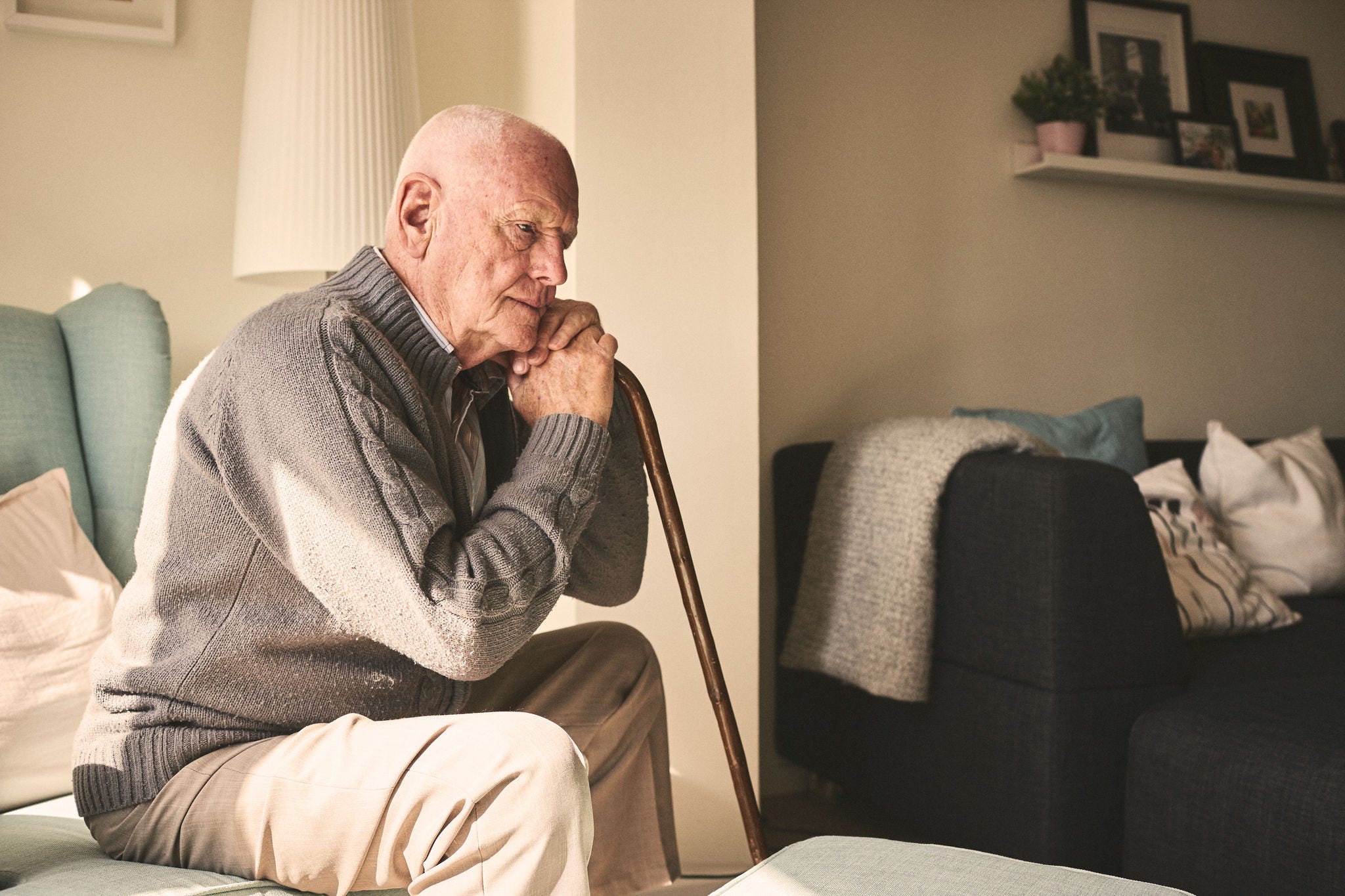 older man sitting alone leaning on cane