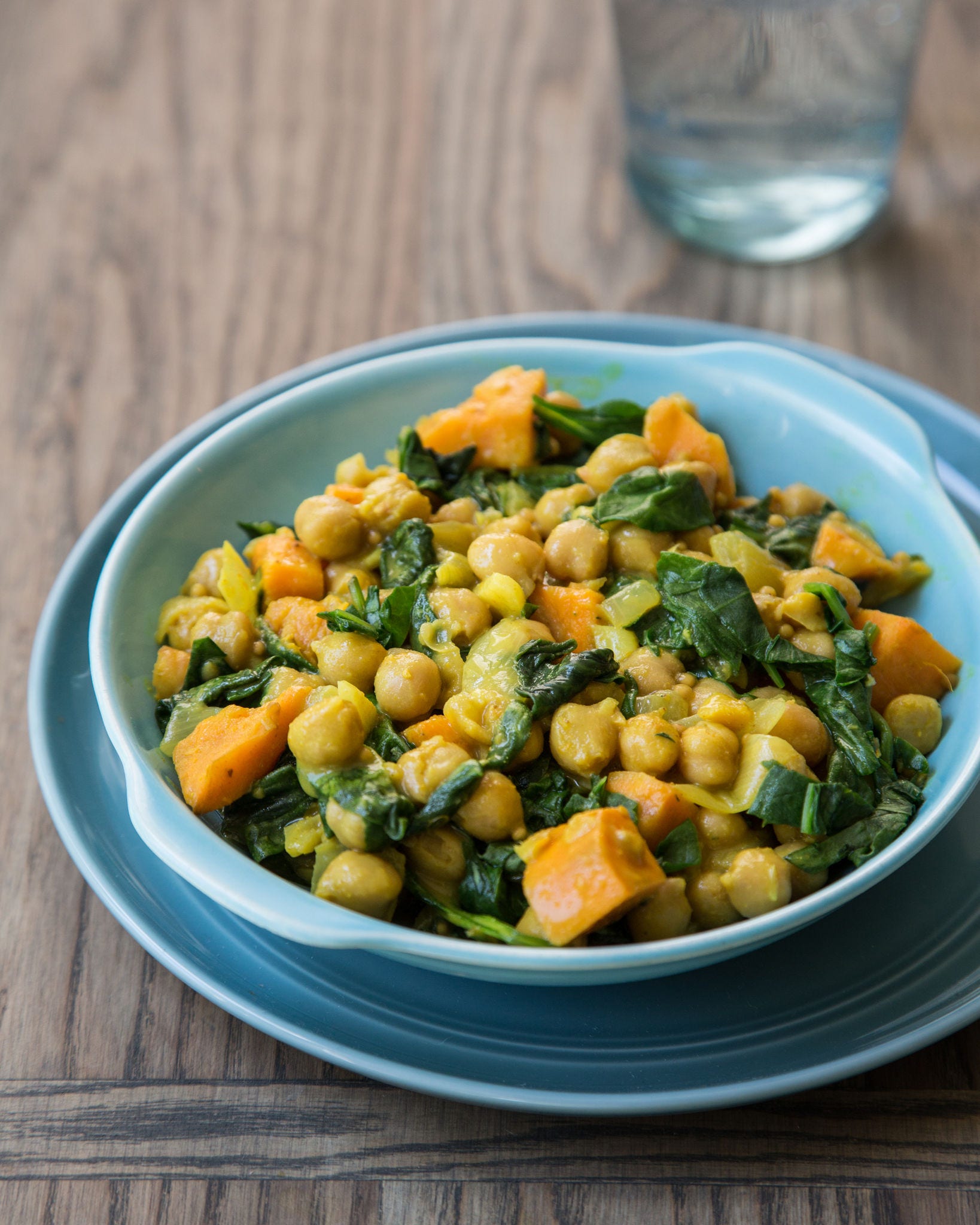 Seen from above, a wooden spoon rests in a pot filled with a chickpea-sweet potato curry.