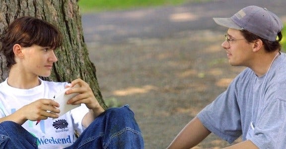 teenage boy and man sitting on ground beside tree talking