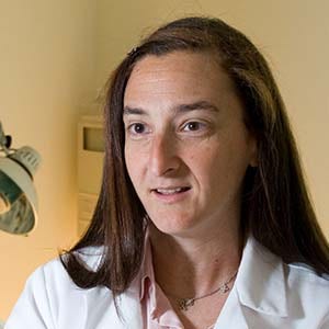 White woman with long brown hair in lab coat with pink shirt