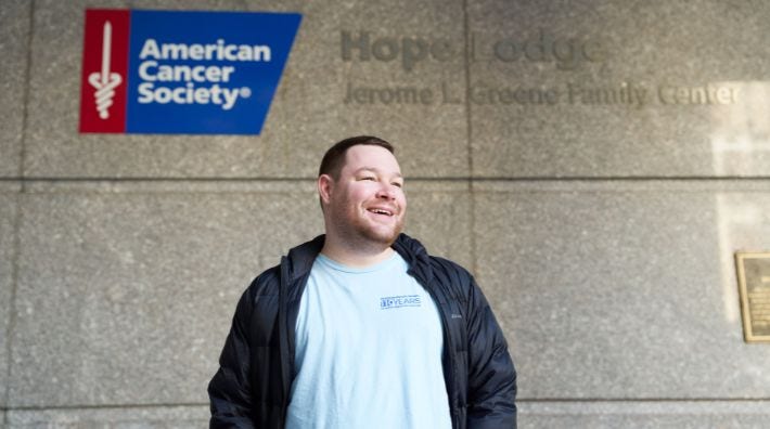 Zach Dane, cancer survivor and volunteer smiling in front of an ACS Hope Lodge