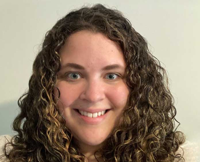 white woman with curly brown hair, longer than shoulders, smiling with teeth showing