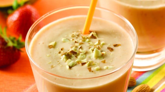 glass of papaya and almond smoothie sitting on table with almonds and strawberries in background