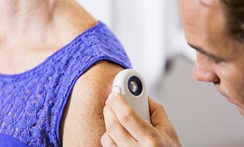 A doctor examining the shoulder skin of a female patient through a device