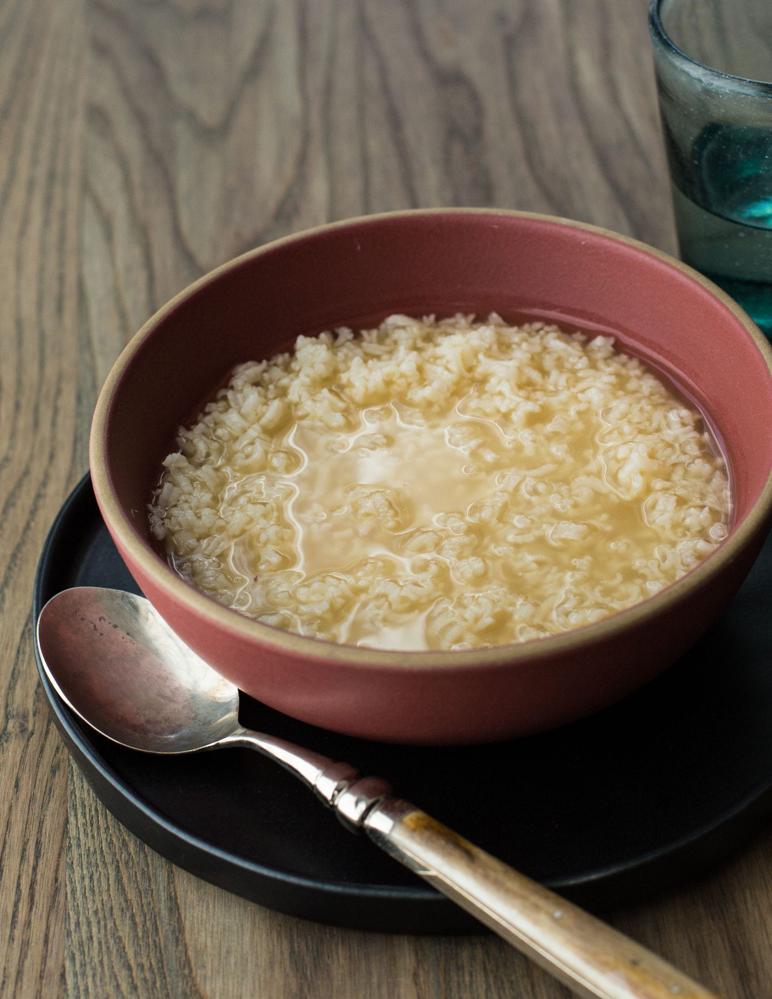 A spoon rests on a plate holding a bowl of chicken congee, made with chicken broth, shredded chicken, ginger, and rice.