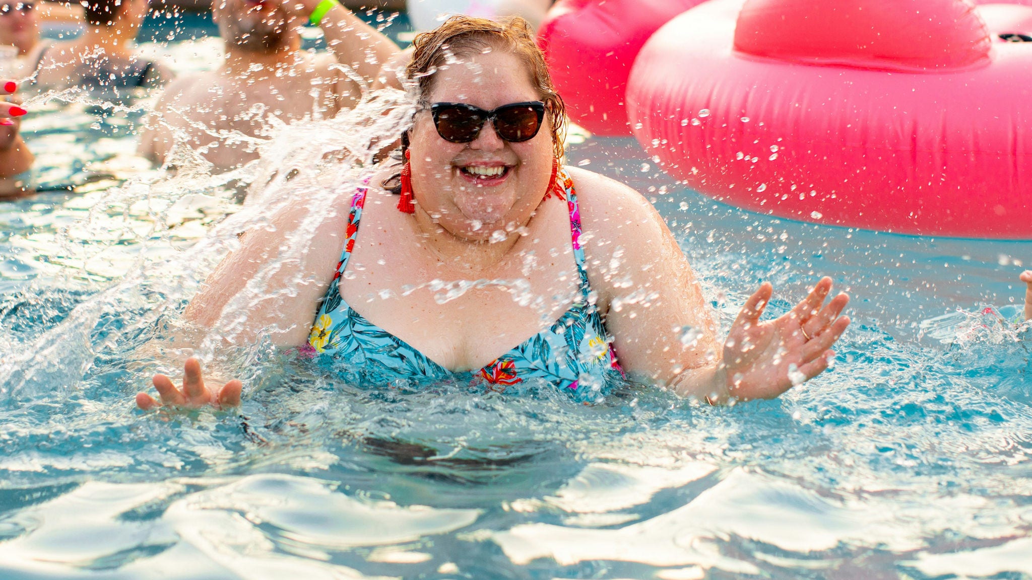 woman with overweight is splashing in pool woman sunglasses orange tassel earrings