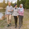 Two older adults walk next to a pond, arm in arm with a younger woman wearing a headscarf.