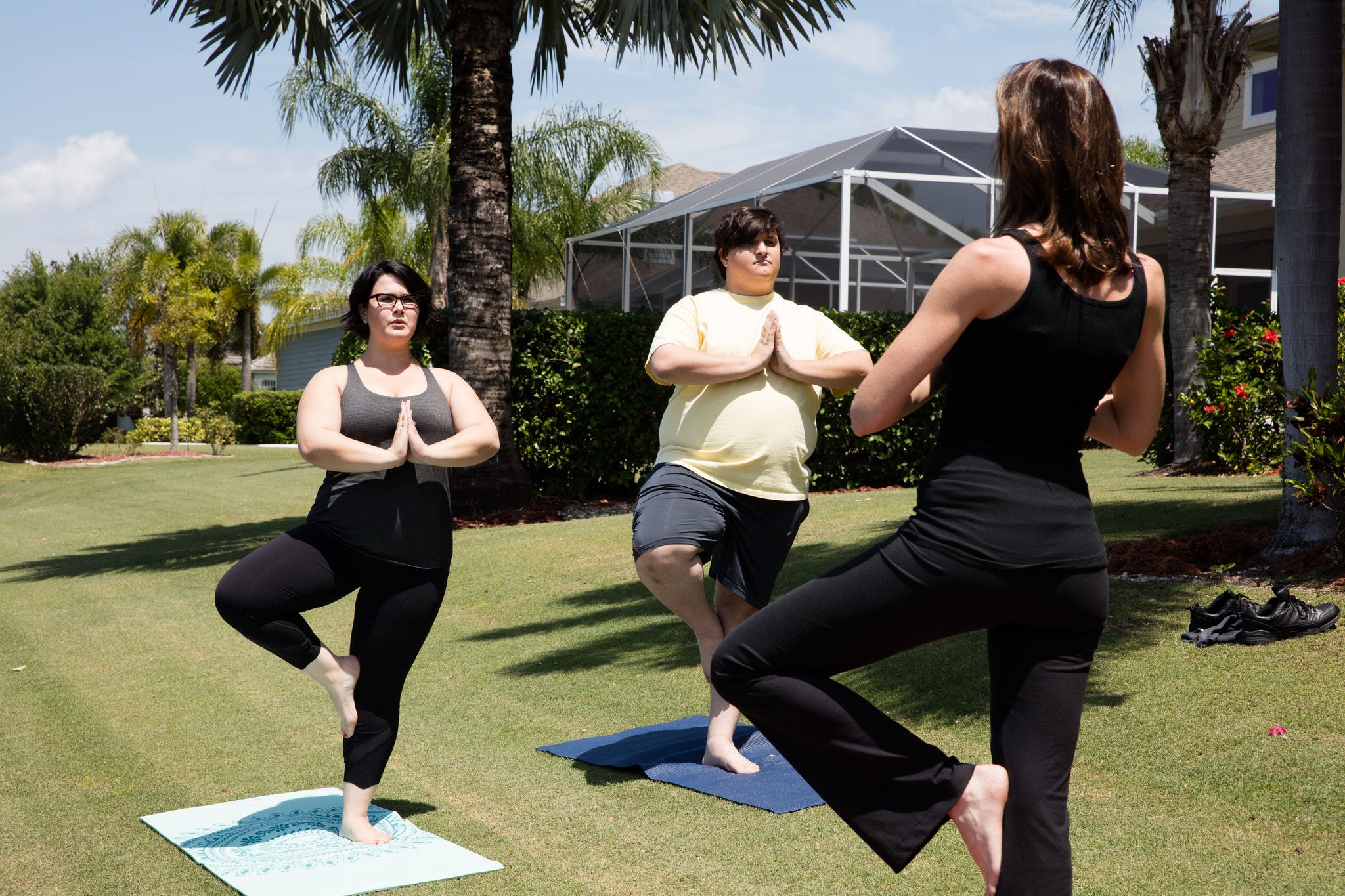 back of thin yoga instructor in black facing a woman and young man in yoga poses both overweight