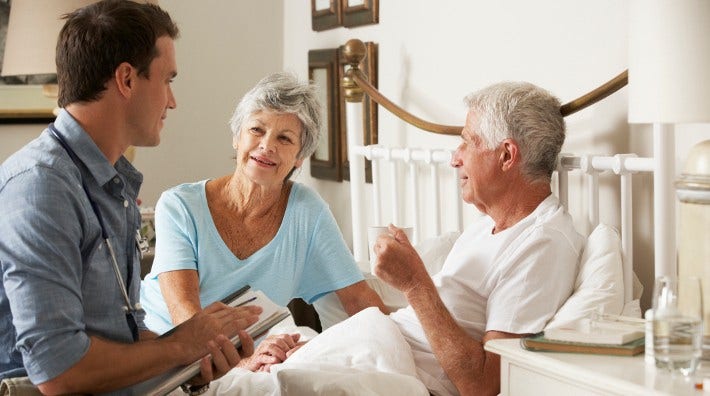 senior man receives in-home medical care from his doctor as his wife watches