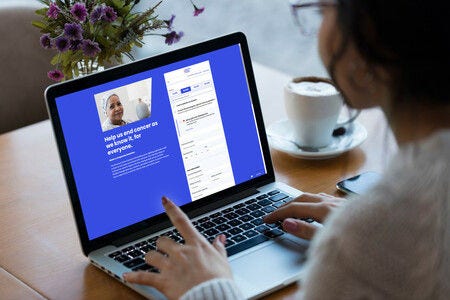 Person using a laptop displaying a cancer awareness donation webpage, with coffee and purple flowers on the table.