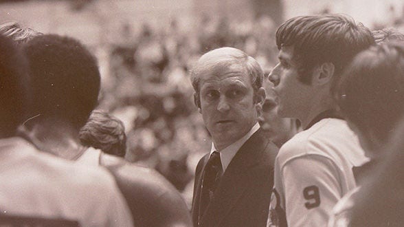 Coach speaking to basketball players during a game huddle.