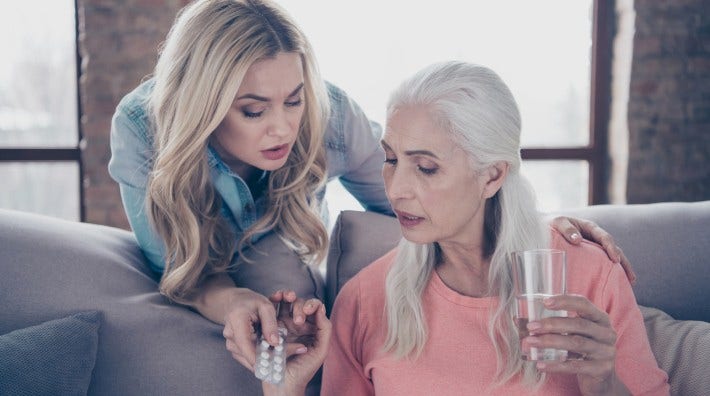 adult daughter helps her mother take medications