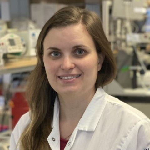 woman with long hair pulled over shoulder of white lab coat, university of california on shoulder