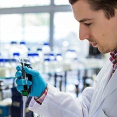 A young male scientist in a white lab coat looks at a vial of blood in a laboratory.