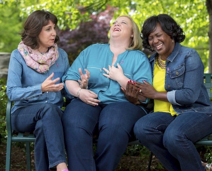 three laughing women sitting on park bench