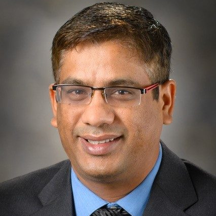 man with rectangular glasses, bright blue shirt, dark gray jacket