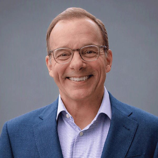 Smiling man wearing glasses and a blue blazer.