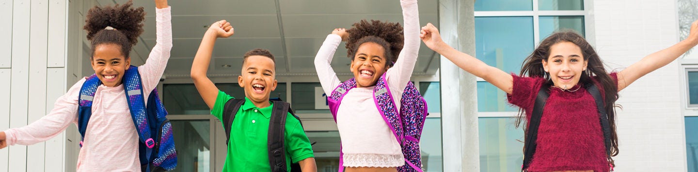 four children jumping for joy with backpacks on