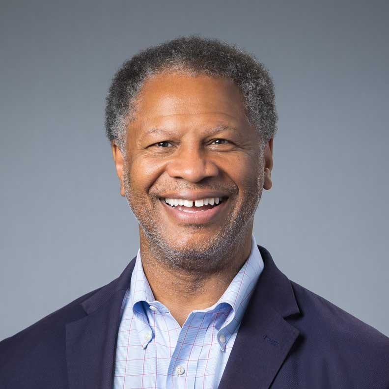 Smiling man in blazer and checkered dress shirt.