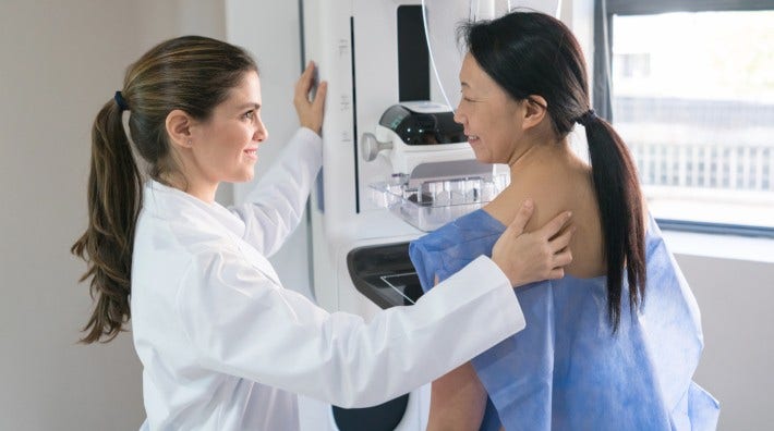 tech or nurse helping a patient get in position for a mammogram  