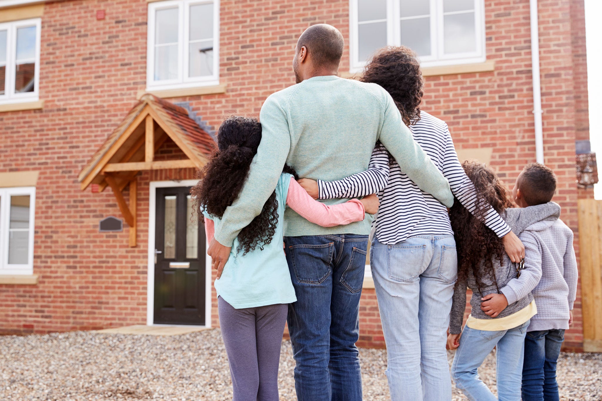 Rear View Of Family Standing Outside New Home On Moving Day Looking At House