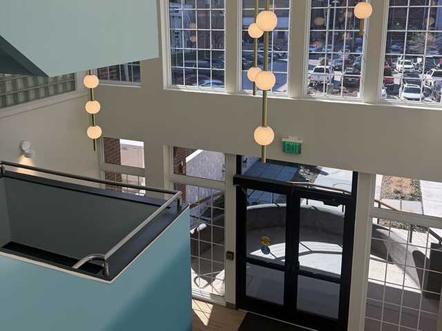 Bright lobby with tall windows, hanging lights, and glass entrance doors.