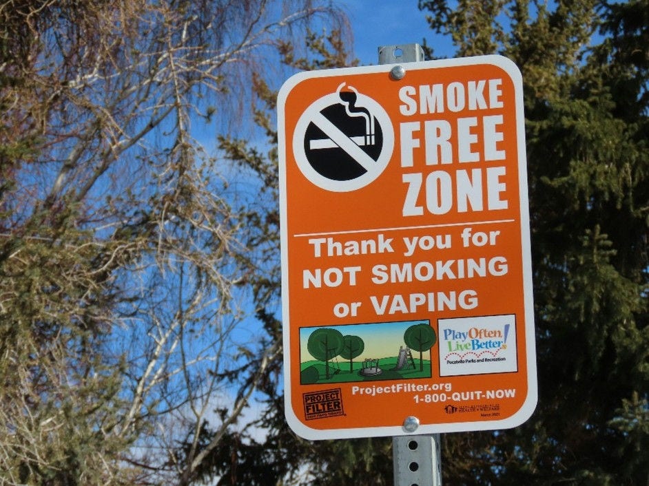 Orange sign in front of trees and blue sky: Thank you for not smoking or vaping