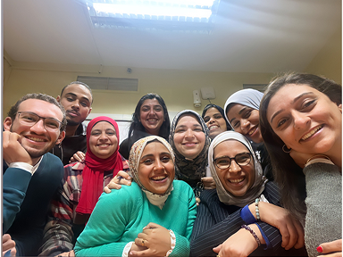 A group of people gather closely indoors, seated and standing around a table