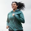 A woman wearing a green jacket and listening to headphones jogs. 