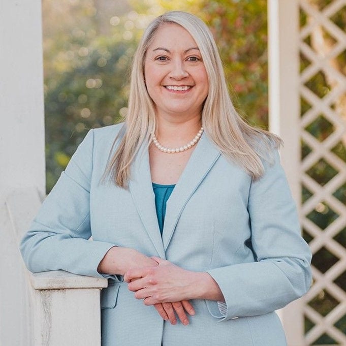 Smiling woman in light blue blazer outdoors.