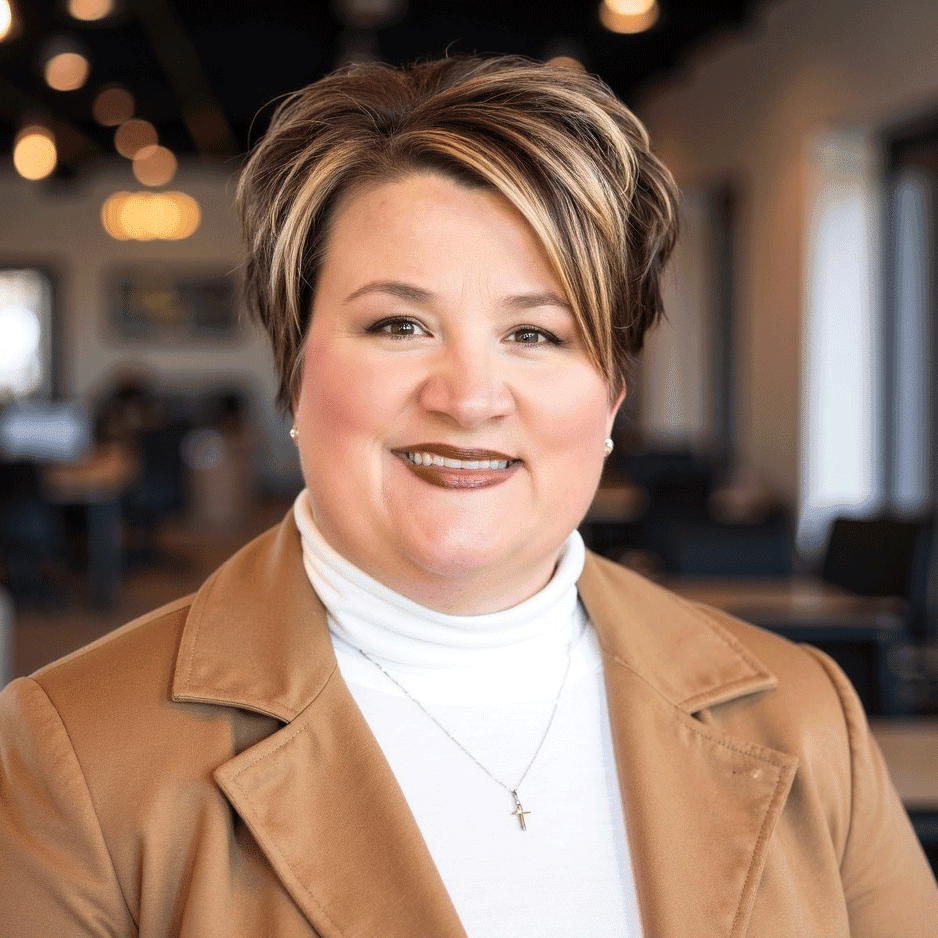 Smiling woman with short highlighted hair wearing tan jacket indoors.