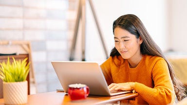 A person seated at a table using a laptop, with a red coffee mug and a small potted plant placed nearby.