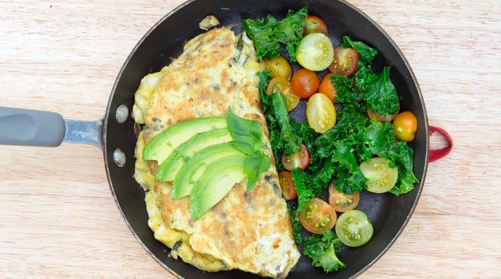frying pan holds vegetable omelet beside greens and tomatoes