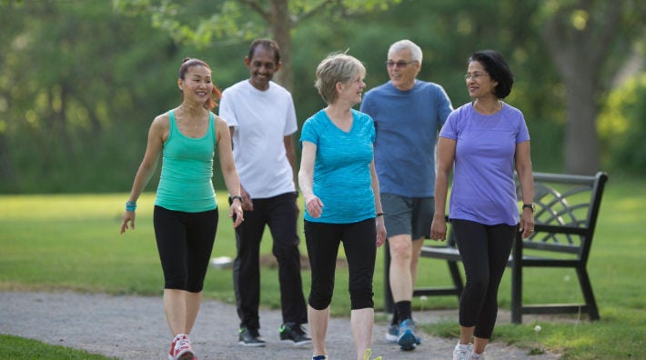 Three woman and two men walk on a park path next to a black bench.