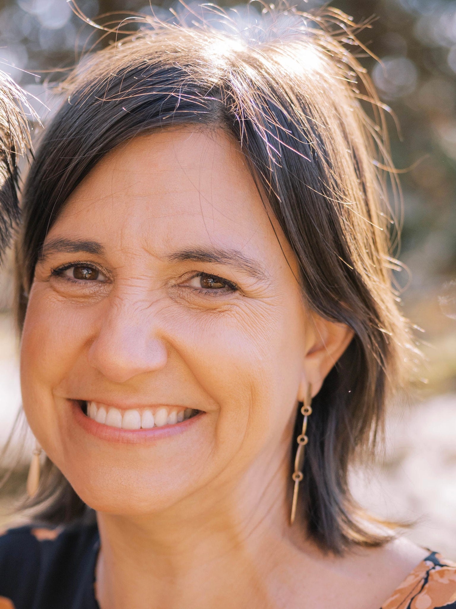 Woman, smiling, short brown hair, dangling earrings, black and orange blouse