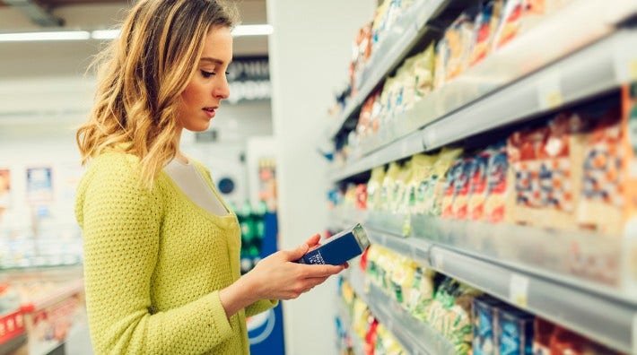 woman reads food label on box in grocery store aisle