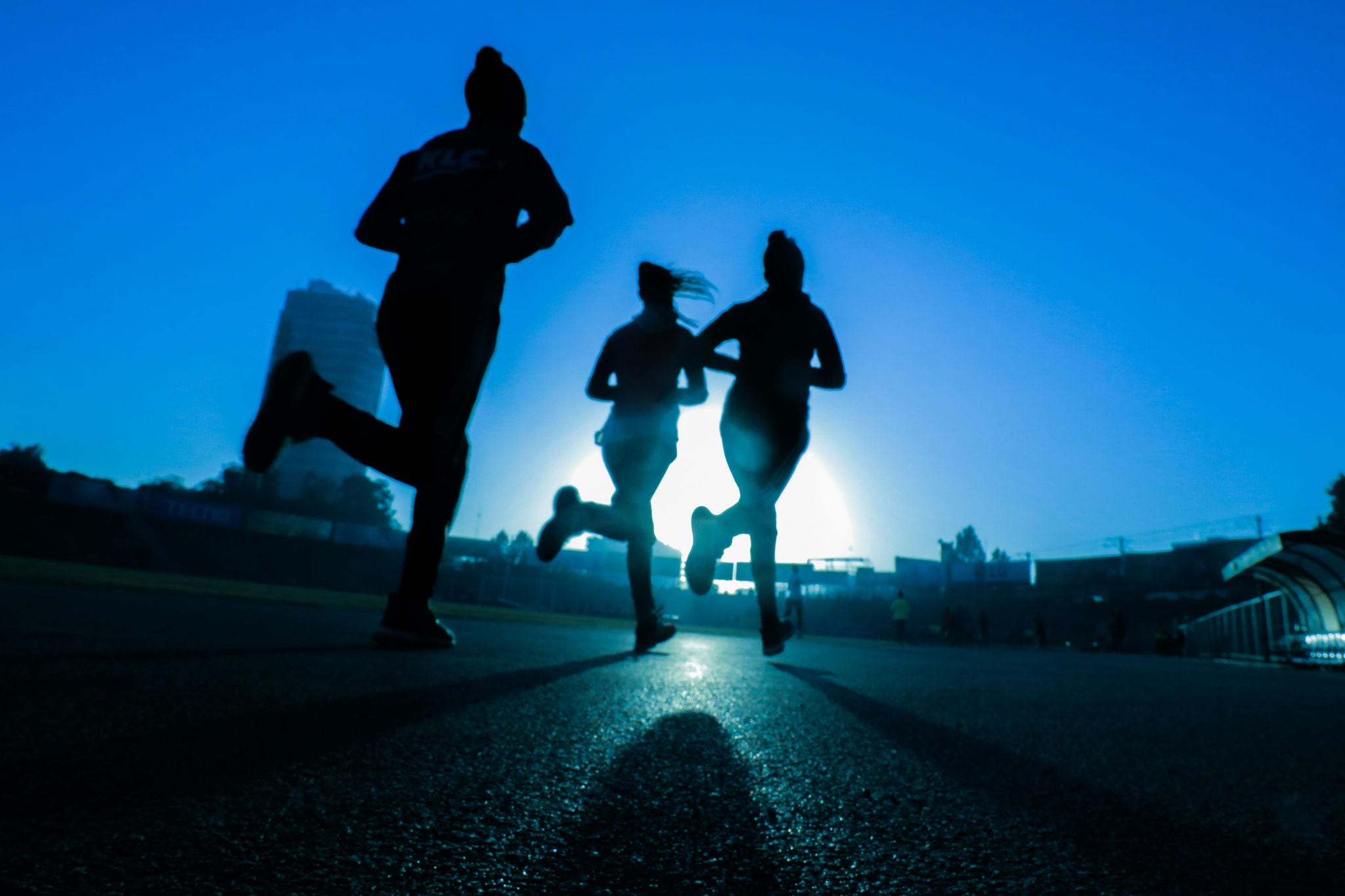 Blue background with white sun and silhouettes of 3 runners