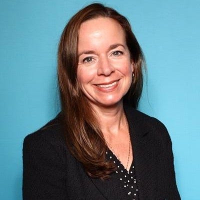 A smiling woman in professional attire against a blue background.