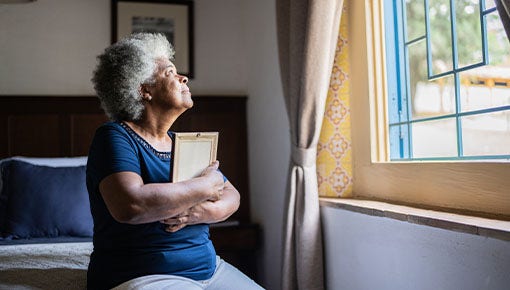 elderly black woman holding a picture while looking out the window