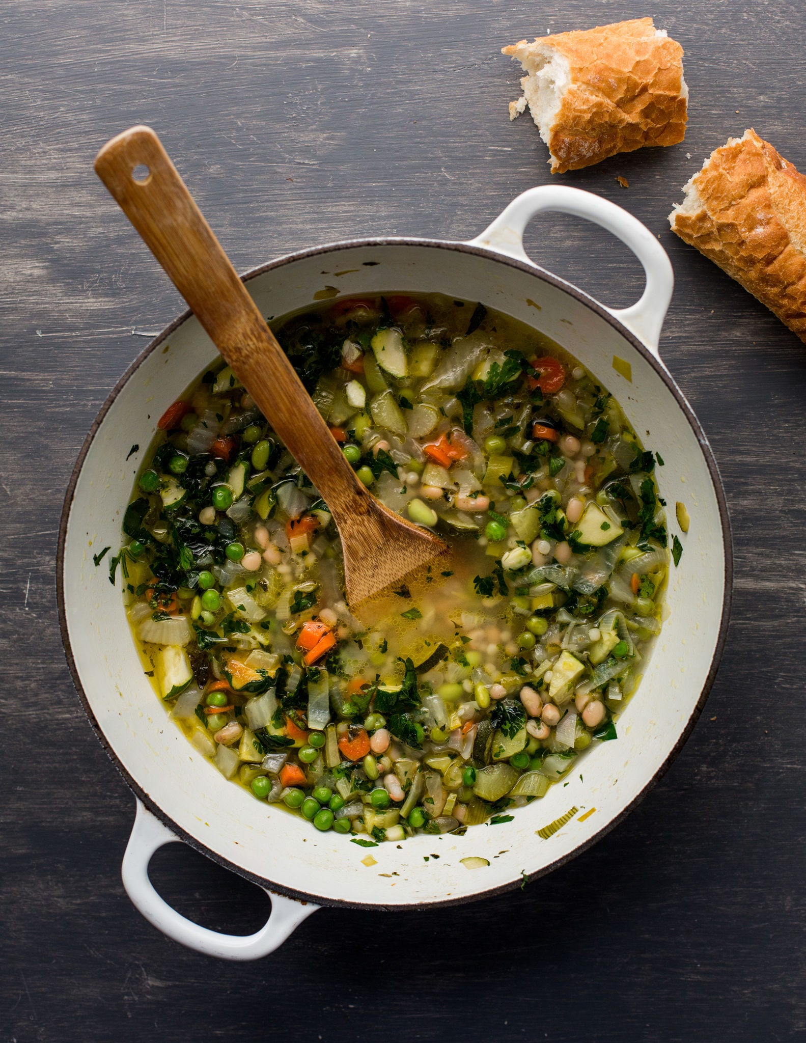 A wooden spoon sticks out of a pot of minestrone seen from overhead.