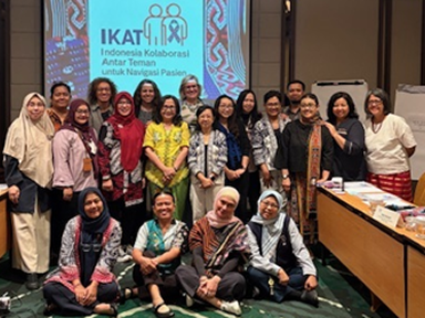 A large group gathered indoors poses in front of a screen displaying “IKAT” and additional text.