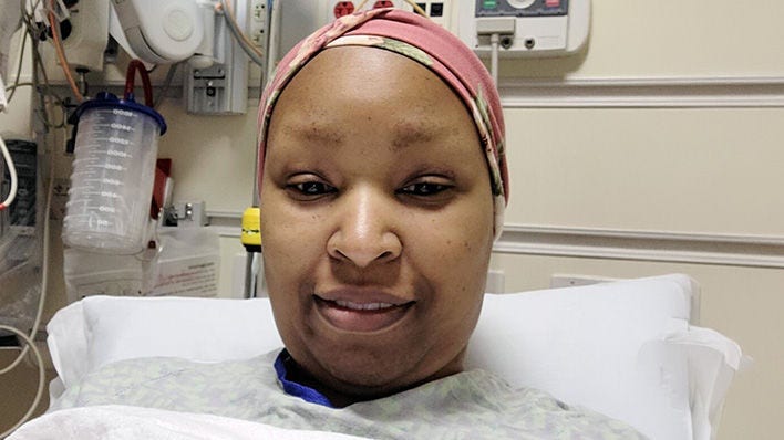 Paciente en una cama de hospital con pañuelo en la cabeza, sonriendo a la cámara.