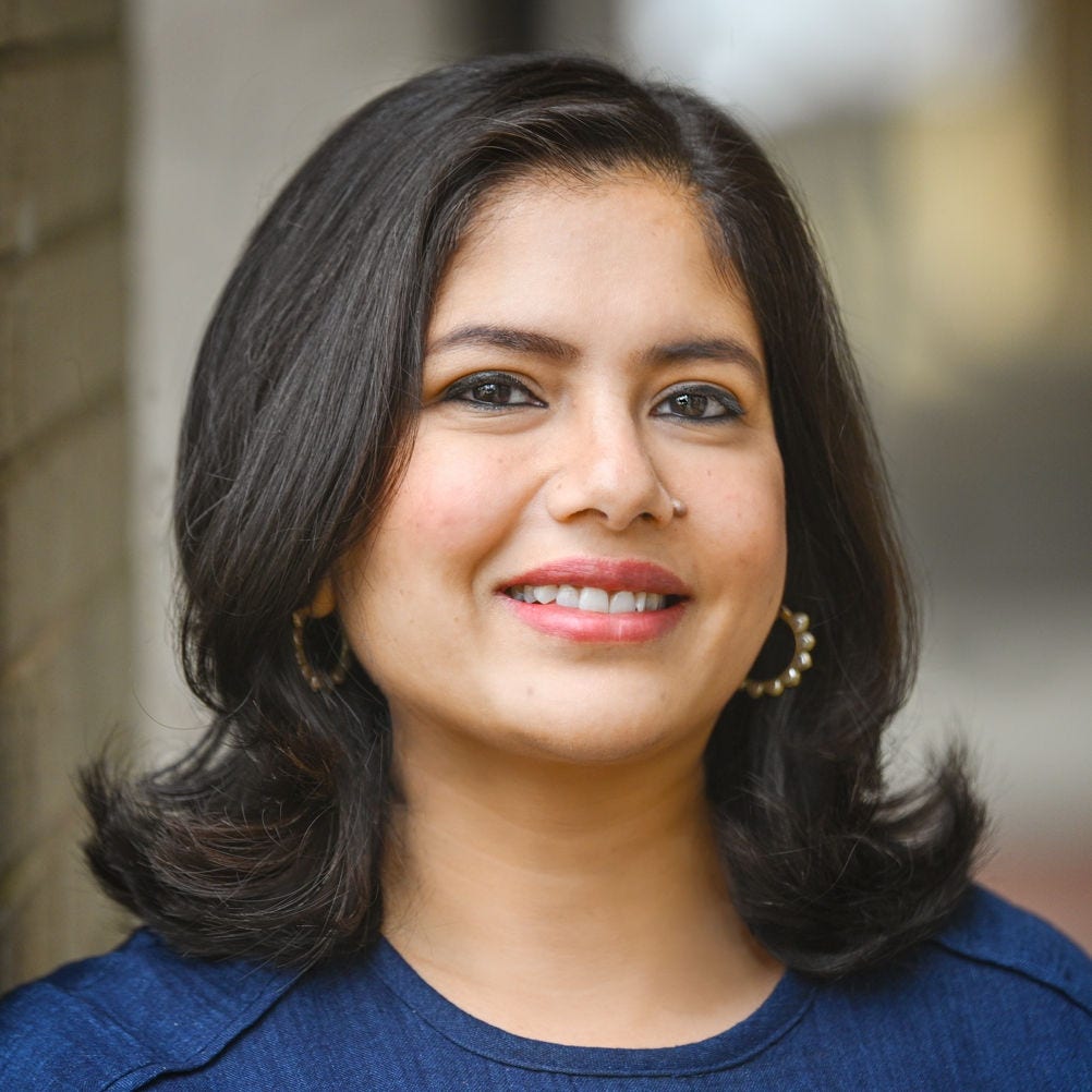 Headshot of Priti Bandi, PhD, in a navy blue blouse, standing in front of a brick wall