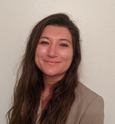 White woman with long brown hair and tan suit jacket